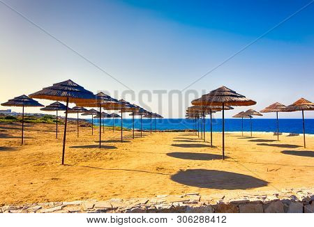 Sand Beach With Rows Of Strawy Beach Umbrellas. Summer Day.