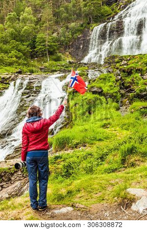 Tourist Woman With Norwegian Flag At Svandalsfossen In Norway, Powerful Waterfall In Norwegian Mount