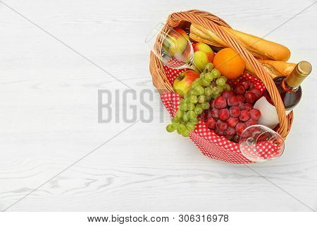 Picnic Basket With Products And Wine On White Wooden Table, Top View. Space For Text