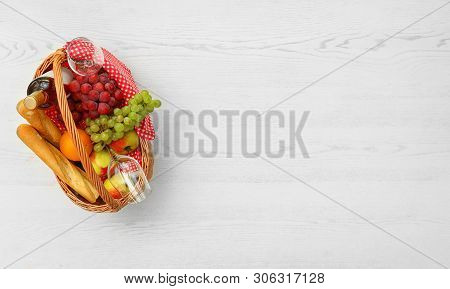 Picnic Basket With Products And Wine On White Wooden Table, Top View. Space For Text