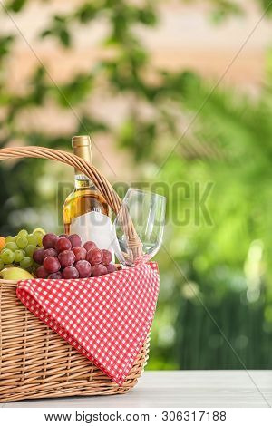 Picnic Basket With Products And Wine On Table Against Blurred Background, Space For Text