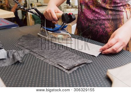 A Woman Strokes The Fabric For Further Sewing. Tailor Ironing Clothes With Industrial Iron.