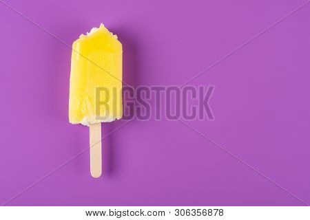 Yellow Popsicle With Couple Of Bites On A Purple Background