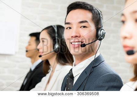 Smiling Male Asian Customer Service Telemarketing Agent Working In Call Center With His Team