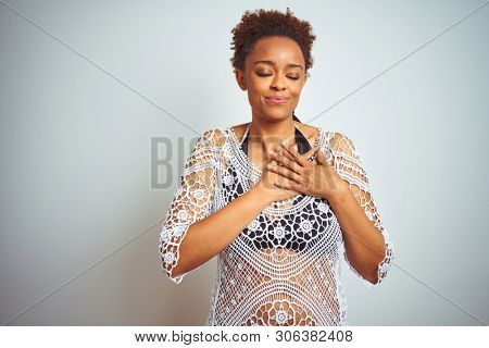 Young african american woman with afro hair wearing a bikini over white isolated background smiling with hands on chest with closed eyes and grateful gesture on face. Health concept.
