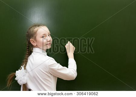 A Girl Of 10-12 Years Old Is Writing On The Blackboard. Schoolgirl Teen With Chalk On A Blackboard W