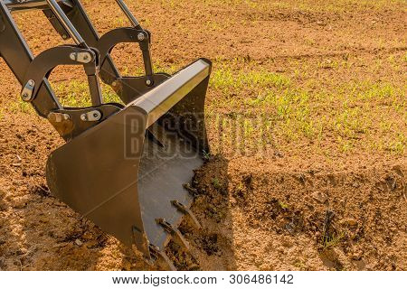 Closeup Of Front End Loader Bucket And Hydraulic Arms In Freshly Planted Field On Sunny Morning.