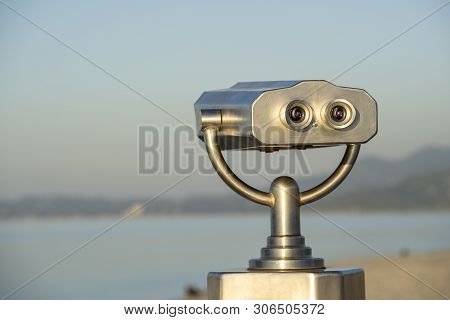 Public Binocular On Sea Shore, Close Up. Coin Operated Binocular Viewer On Blurred Background Of Sun