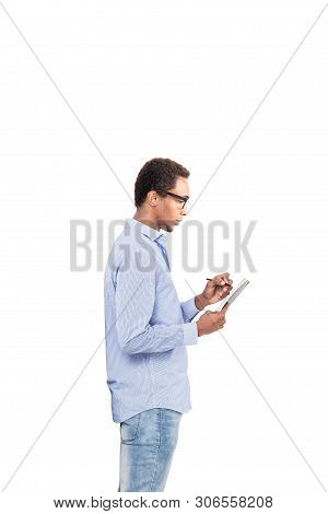 Side View Of Serious Young African American Man In Blue Shirt, Jeans And Glasses Taking Notes. Isola