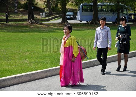 Pyongyang, North Korea - May 1, 2019: An Old Woman In Traditional Korean Clothes And A Young Couple 