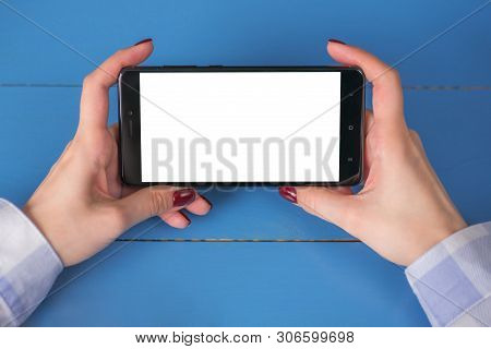 Mockup Image: Woman Looking At Black Smartphone With White Blank Screen On Blue Table. Close Up View