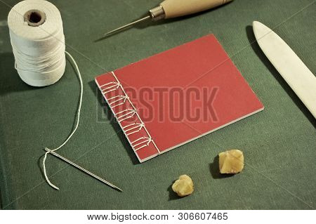 Small Red Stab Stitch Book Surrounded By Bookbinding Tools