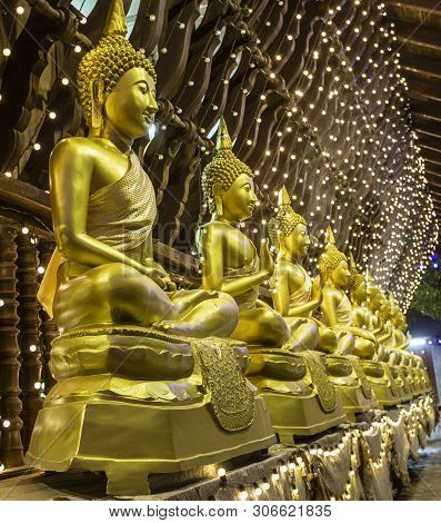 Row Of Golden Buddha Statues Sitting On Pillows In Seema Malaka Temple - End View.