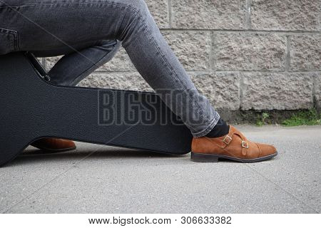 Man Put His Foot On A Hard Guitar Case. Hard Case For Electric Guitar. Man Dressed In Jeans Holding 