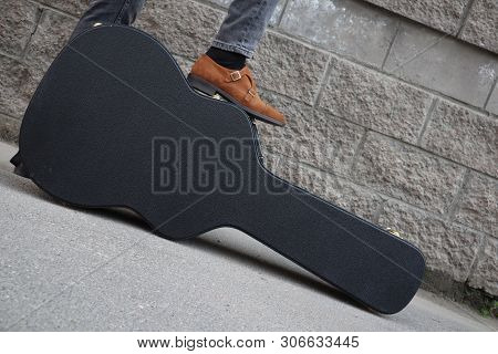 Man Put His Foot On A Hard Guitar Case. Hard Case For Electric Guitar. Man Dressed In Jeans Holding 