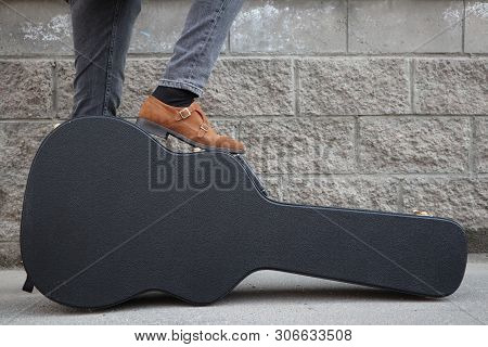 Man Put His Foot On A Hard Guitar Case. Hard Case For Electric Guitar. Man Dressed In Jeans Holding 
