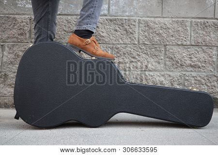 Man Put His Foot On A Hard Guitar Case. Hard Case For Electric Guitar. Man Dressed In Jeans Holding 