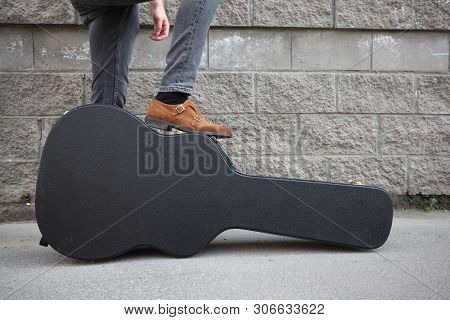 Man Put His Foot On A Hard Guitar Case. Hard Case For Electric Guitar. Man Dressed In Jeans Holding 