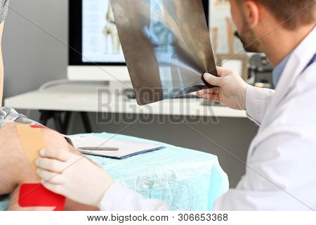 Smart Doctor Looking At X-ray Picture Of Patients Injured Leg. Concentrated Doc Man Touching Trouble