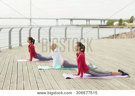 Side View Portrait Of Three Contemporary Women Doing Yoga And Stretching On Riverside Outdoors, Copy