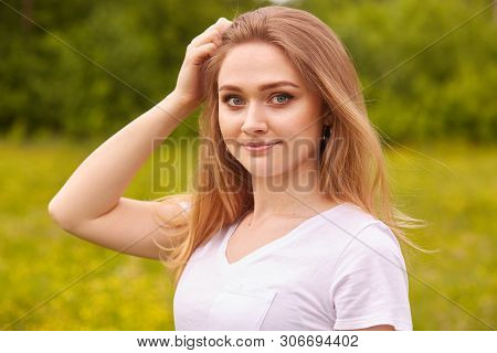 Close Up Portrait Of Young Beautiful Blonde Woman With Staright Hair, Posing In Meadow In Sunny Summ