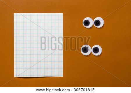 Pair Of Google Eyes Are Looking At Sheet Of Notebook With Copy Space For Your Text, On A Brown Paper