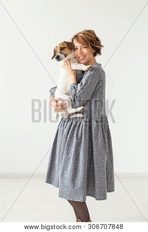 Charming Smiling Young Woman In A Stylish Gray Dress Holding Her Favorite Dog Jack Russell Terrier. 