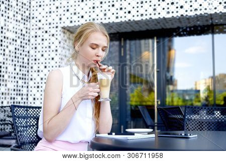 Young Woman Having Coffee Break Sitting At Cafe And Drinking Latte Through Straw