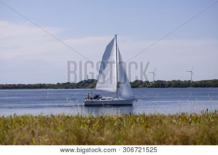 Sailboat For Full Sail On A River On A Sunny Day With Wind Turbines In The Background. Copenhagen, D