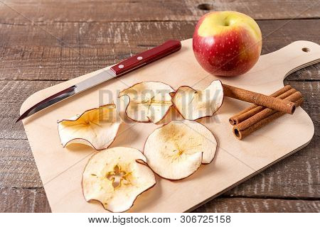 Front View Dried Apple Chips , Raw Apple , Cinnamon Sticks On Cooking Board Over Wood Background.