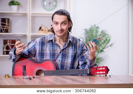 Young handsome repairman repairing guitar