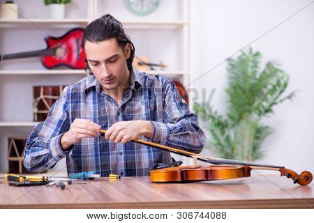 Young handsome repairman repairing violin