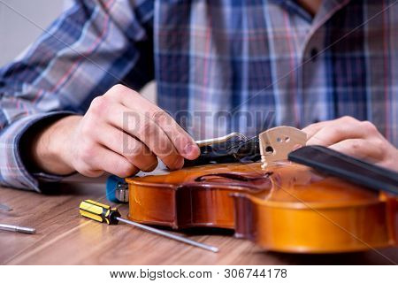 Young handsome repairman repairing violin