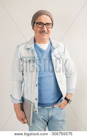 Casual mature man in blue jeans and pullover, white jacket, eyeglasses and beanie standing in front of camera over white background