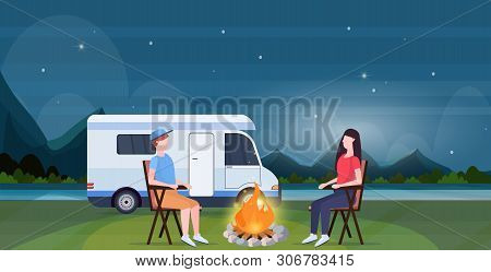 Couple Sitting Around Campfire At Night Near Camping Trailer Truck Caravan Car Man Woman Spendingtim