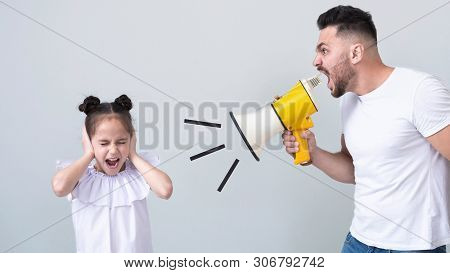 Domestic Tyranny. Furious Dad Screaming At His Daughter With Megaphone, Scared Child Close Her Eyes 