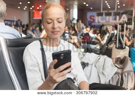 Female Traveler Reading On Her Cell Phone While Waiting To Board A Plane At Departure Gates At Airpo