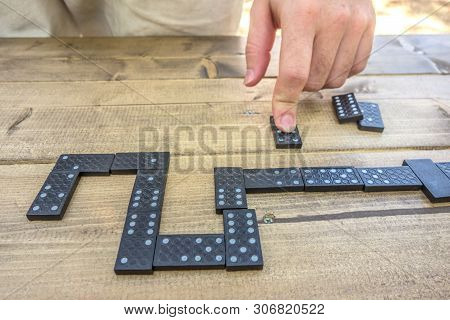 Man's Hand On A Domino On A Wooden Table Background