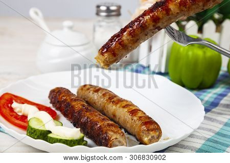 Kupaty In A White Plate And Vegetables On A Wooden Table. Sausages Grill. Tasty Food.
