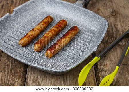 Kupaty In A Frying Pan On A Wooden Table. Sausages Grill. Tasty Food.