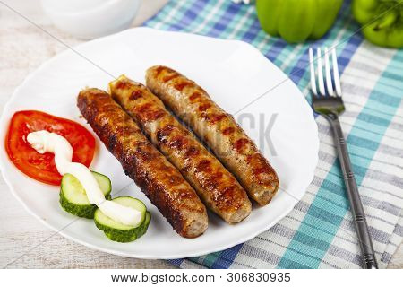 Kupaty In A White Plate And Vegetables On A Wooden Table. Sausages Grill. Tasty Food.