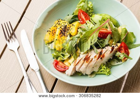 Salad With Grilled Chicken, Mango, Lettuce, Avocado, Tomatoes, Arugula, Cheese Sause On A White Plat
