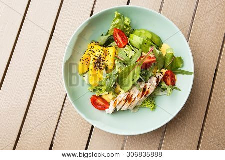 Salad With Grilled Chicken, Mango, Lettuce, Avocado, Tomatoes, Arugula, Cheese Sause On A White Plat