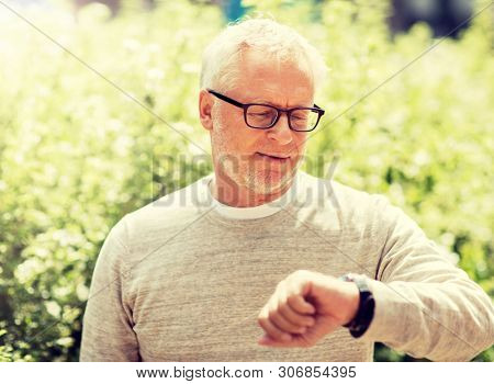 punctuality and people concept - senior man checking time on wristwatch or smart watch on his hand outdoors