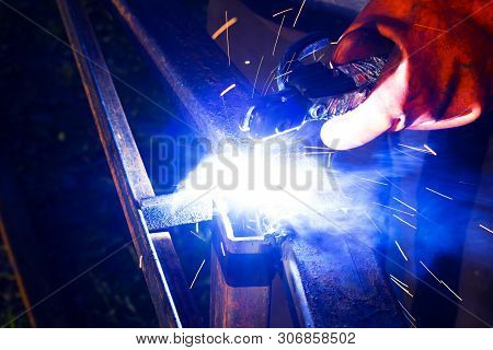Welder Worker Performs Jump Welding. Man Welder In Protective Gloves Performs Arc-welding Process Of