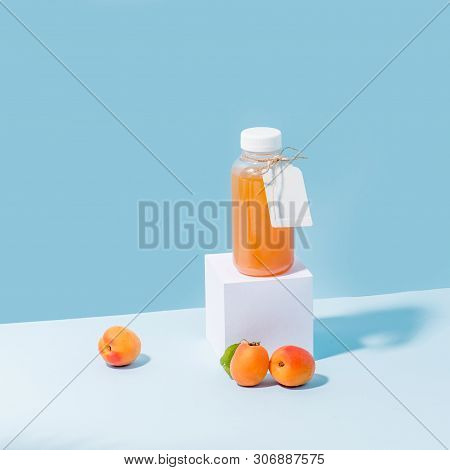 Peach Juice In A Bottle On White Paper Pedestal And Fresh Apricots At Foundation In The Corner Over 