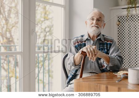 Positive Senior Grandfather With Grey Hair And Beard Sitting At Home
