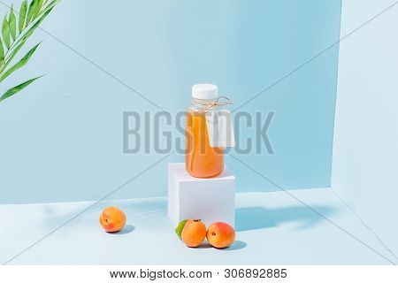 Peach Juice In A Bottle On White Paper Pedestal And Fresh Apricots At Foundation In The Corner Over 