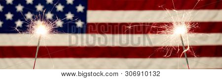 Lit sparklers in front the American Flag for 4th of July celebration