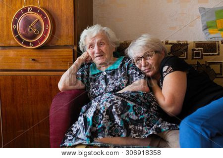 Russian old woman with her adult daughter sitting together at home watching on TV Putin's speech.